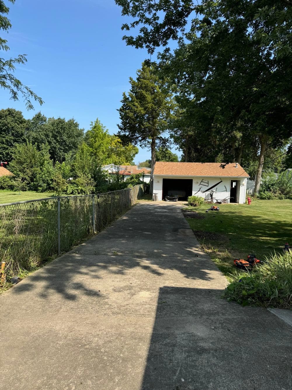 Concrete path leading to a garage surrounded by greenery and trees under a blue sky.