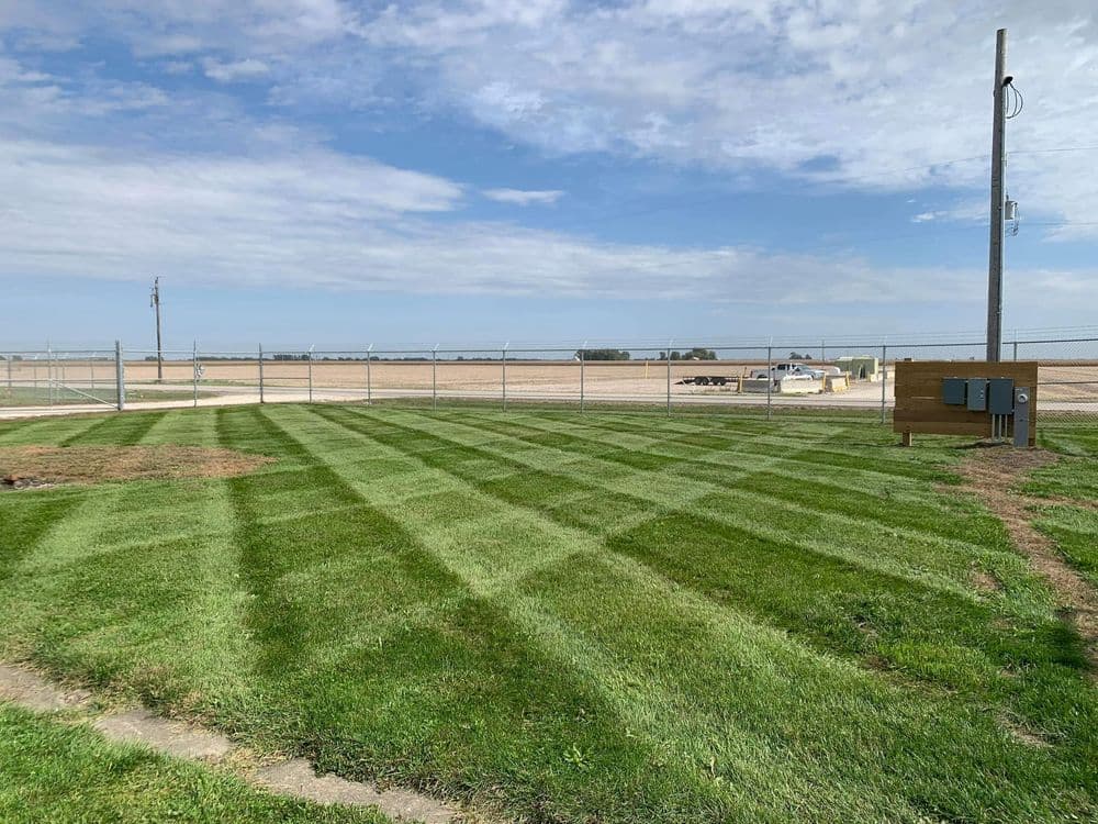 Lush green lawn with striped mowing pattern and distant farm fields under a cloudy sky.