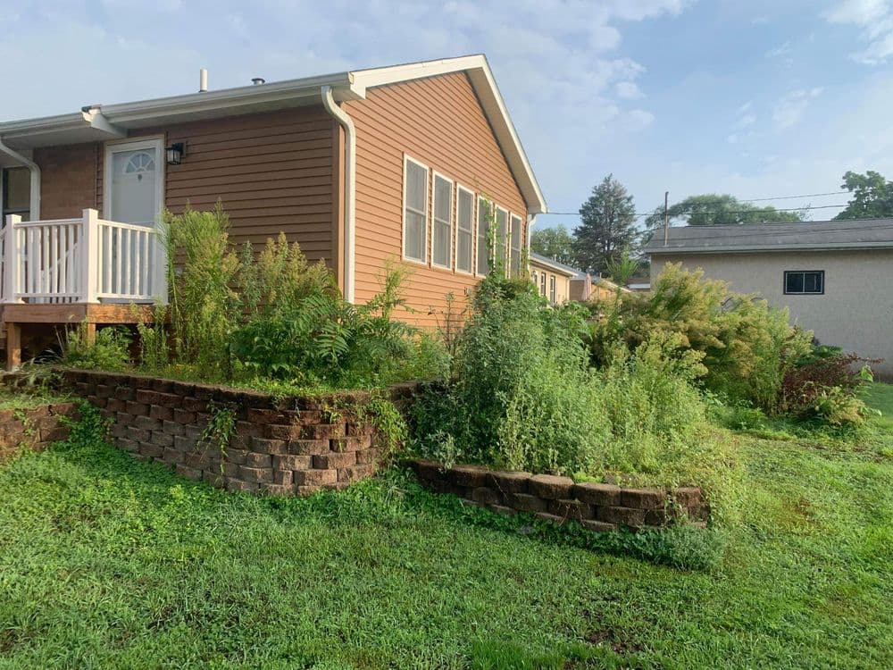 House exterior with landscaped garden and greenery, featuring a stone retaining wall.