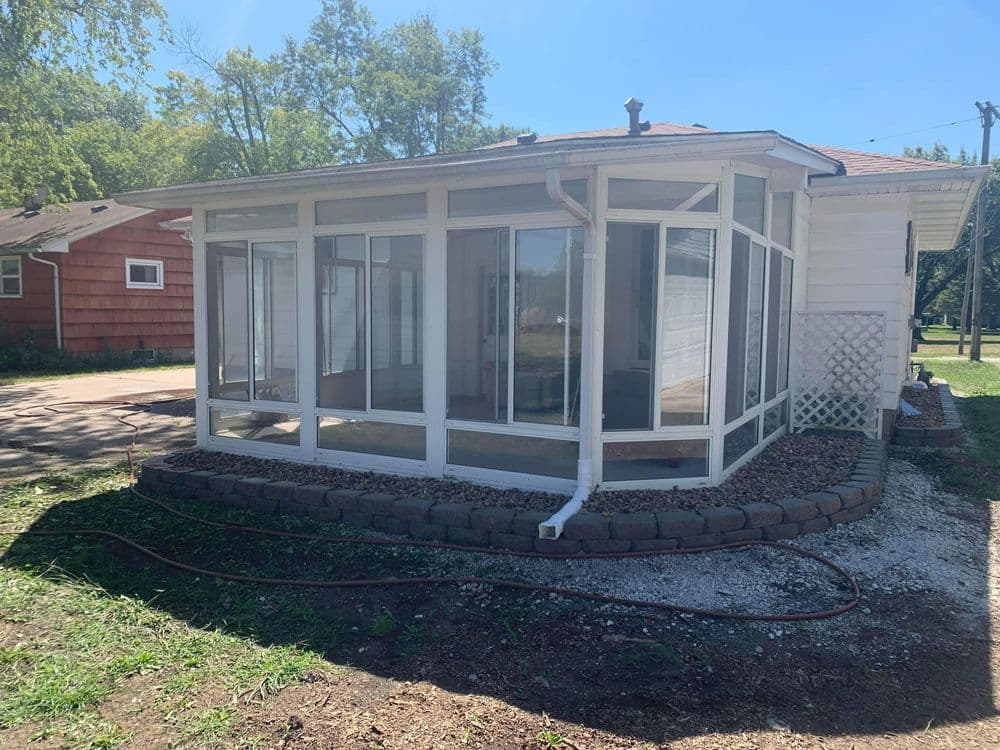 Sunlit screened porch with clear windows, surrounded by garden and pathway. Ideal for relaxation.
