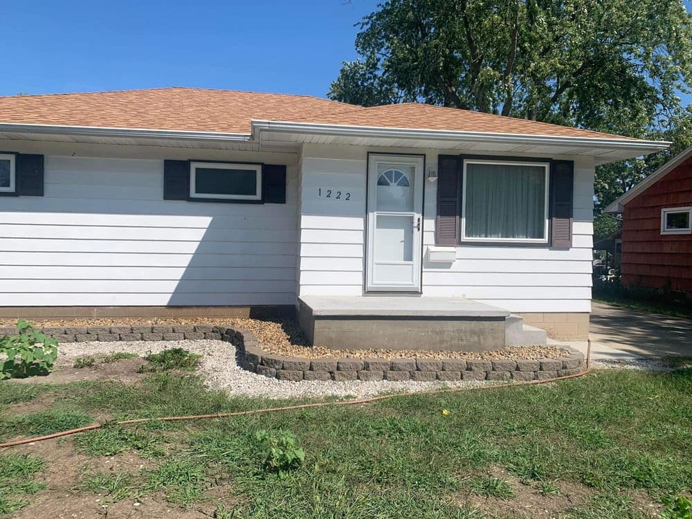 Front view of a single-story home with a brown roof, white siding, and a bright entrance.