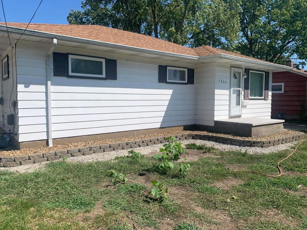 Single-story white house with brown roof, garden area, and clear blue sky backdrop.