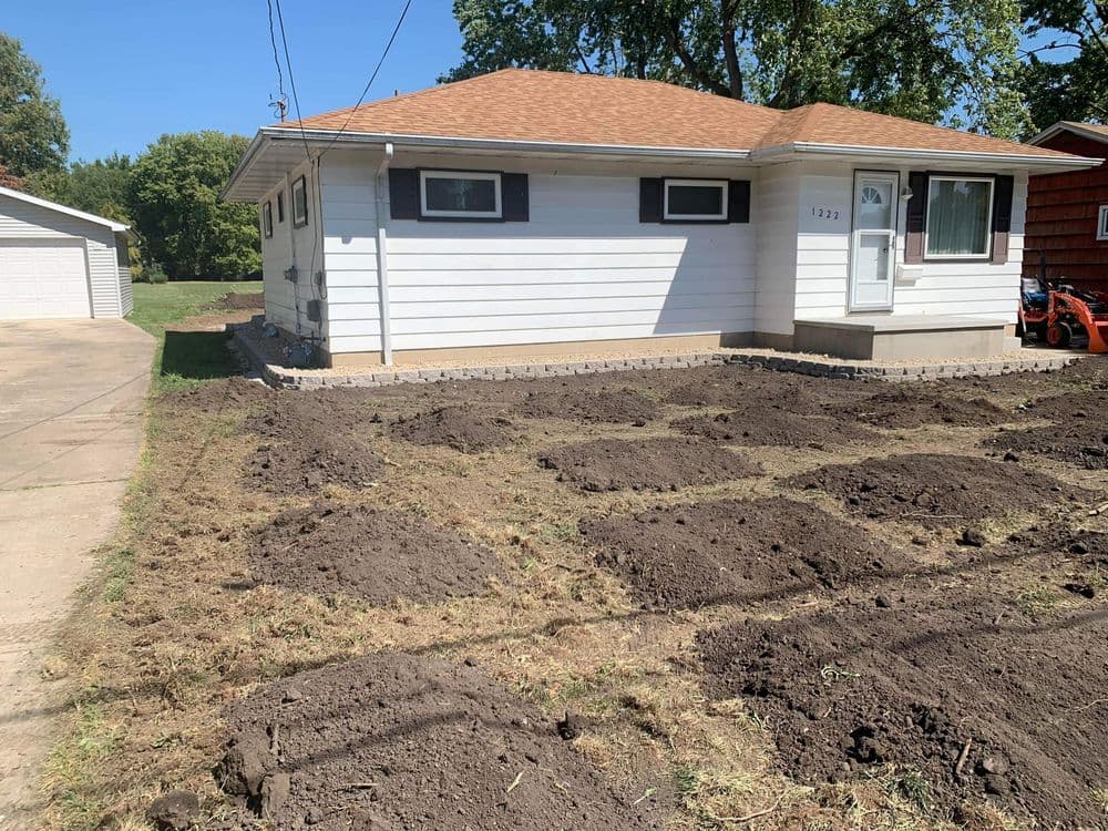 Freshly tilled garden beds in front of a single-story home with a new roof.