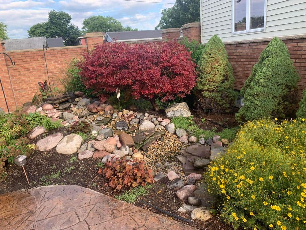 Lush garden with colorful plants, a water feature, and stone pathways in a residential backyard.