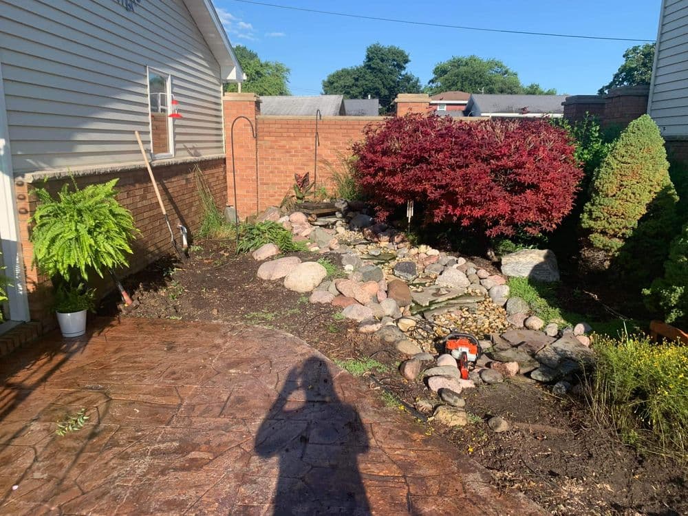 Landscaped garden featuring a rock pond, plants, and a blooming red maple tree.