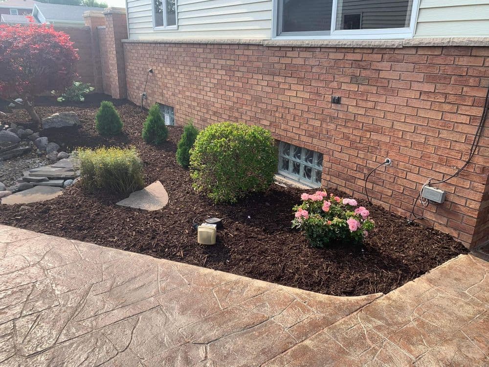 Landscaped garden with brick wall, decorative shrubs, and pink flowers on mulch bed.